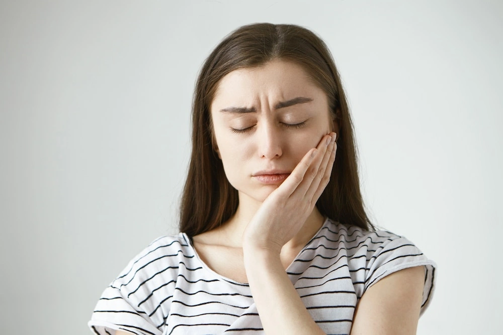 A young woman holding her cheek in pain due to a severe toothache, highlighting a dental emergency.